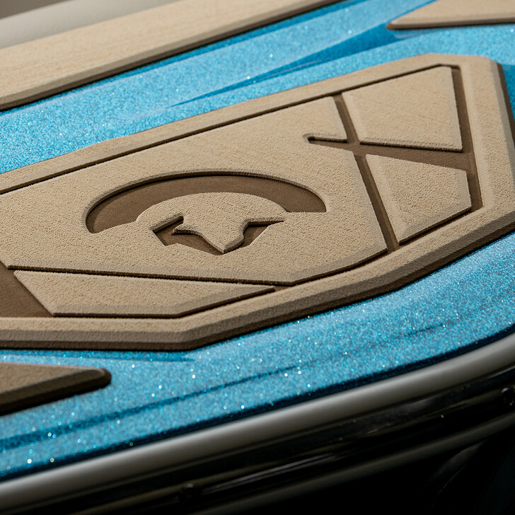 Close-up of a blue, glittery surface with tan, textured padding featuring geometric shapes and a cutout of a stylized animal logo.