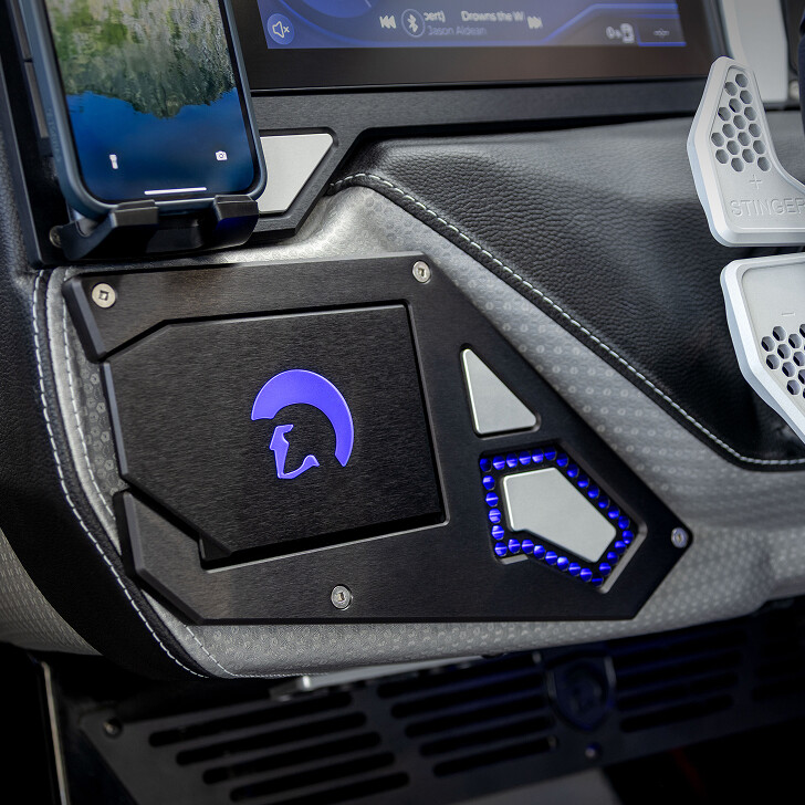 Close-up of a car dashboard featuring a smartphone holder, a display screen, illuminated buttons, and a panel with a helmet logo and blue LED lighting.