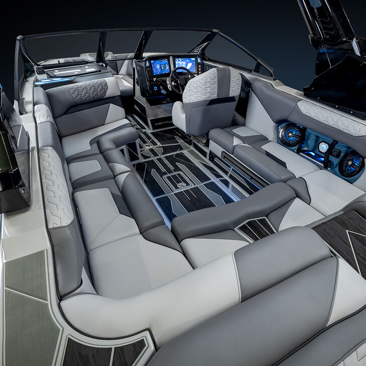 Interior of a modern speedboat featuring gray and white cushioned seating, digital dashboard, built-in speakers, and sleek, geometric flooring.