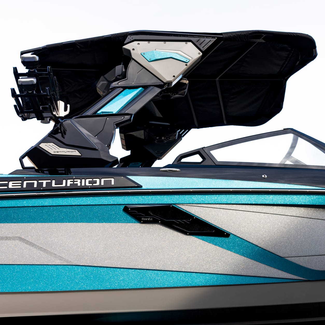 A close-up view of the blue and silver Centurion Ri230, focusing on the upper section of this premium wake boat with a black canopy and support structure.