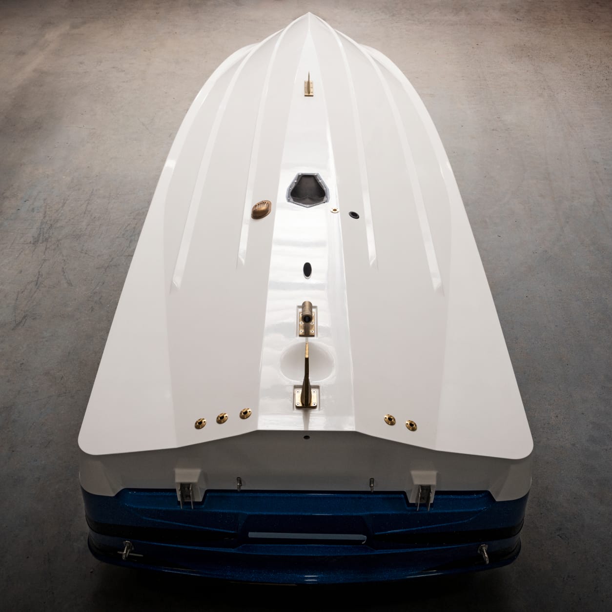 The image shows the underside of a white Centurion Ri230 boat hull with blue trim, viewed from the stern, displaying the keel, hardware, and fittings on a concrete surface.