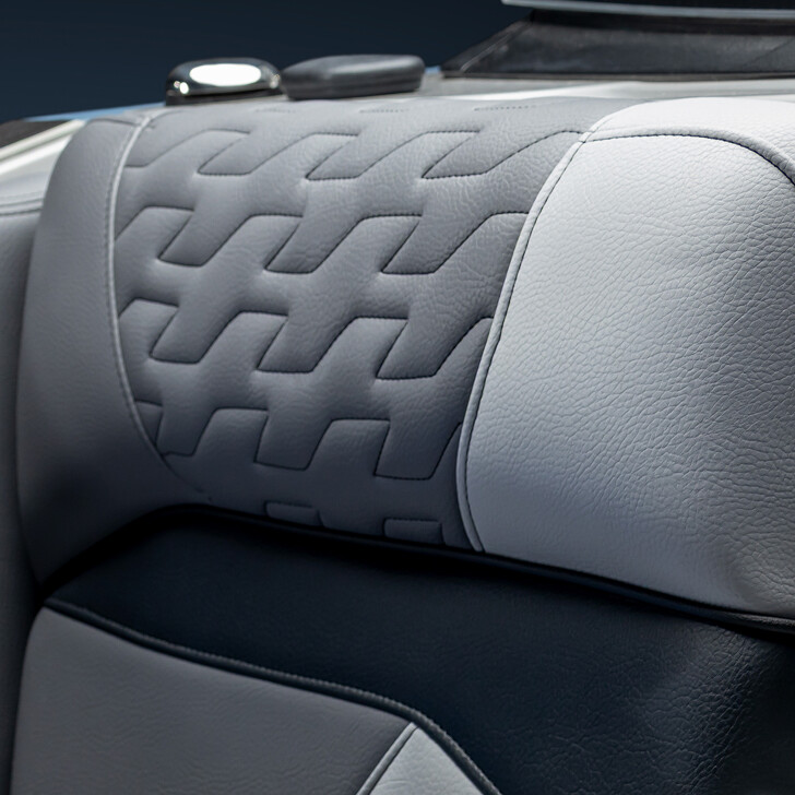 Close-up of a car seat with light and dark grey leather upholstery featuring a stitched, geometric pattern on the upper backrest.