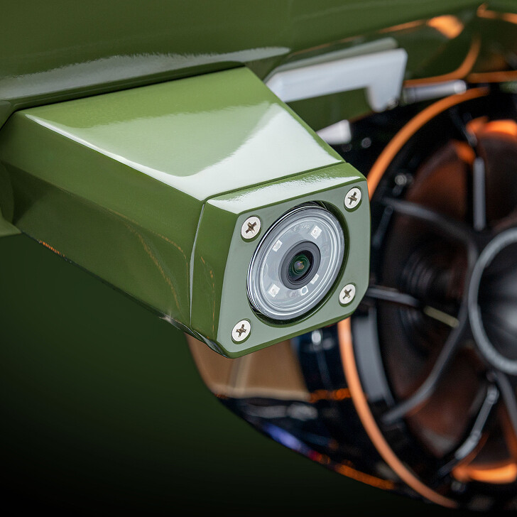 Close-up of a green rearview camera mounted near a wheel rim with orange accents.