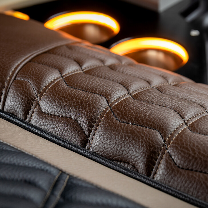 Close-up of brown and black stitched leather car seat with illuminated cup holders in the background.
