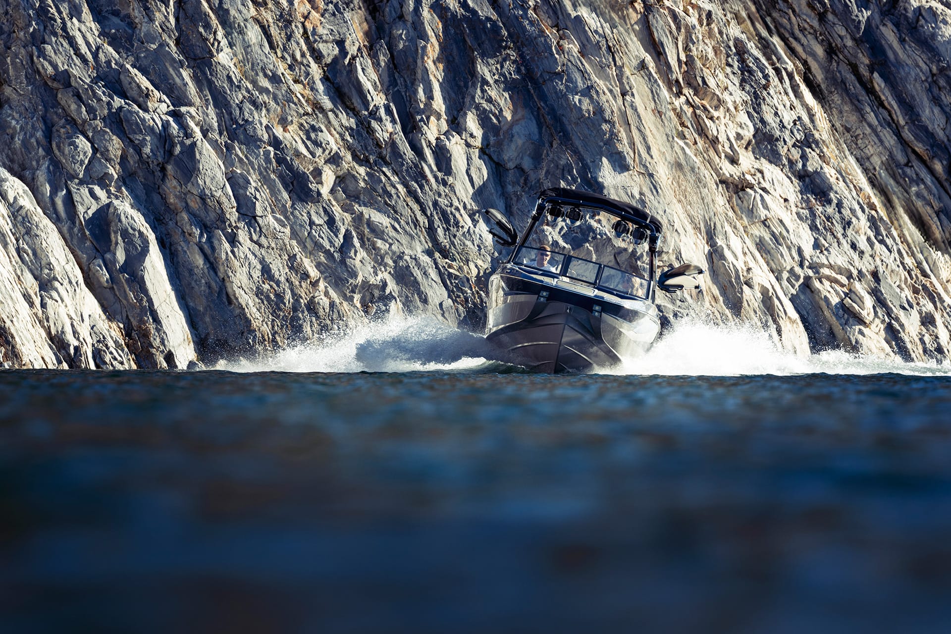 A Centurion Fi23 speeds near a rocky cliff, creating waves as the sleek black motorboat carves through the water.