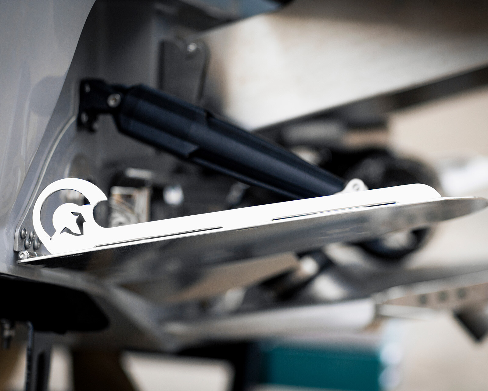 Close-up view of a Centurion Ri245 surf boat’s metal trim tab with a hydraulic actuator, featuring a stylized logo cutout on the bracket.