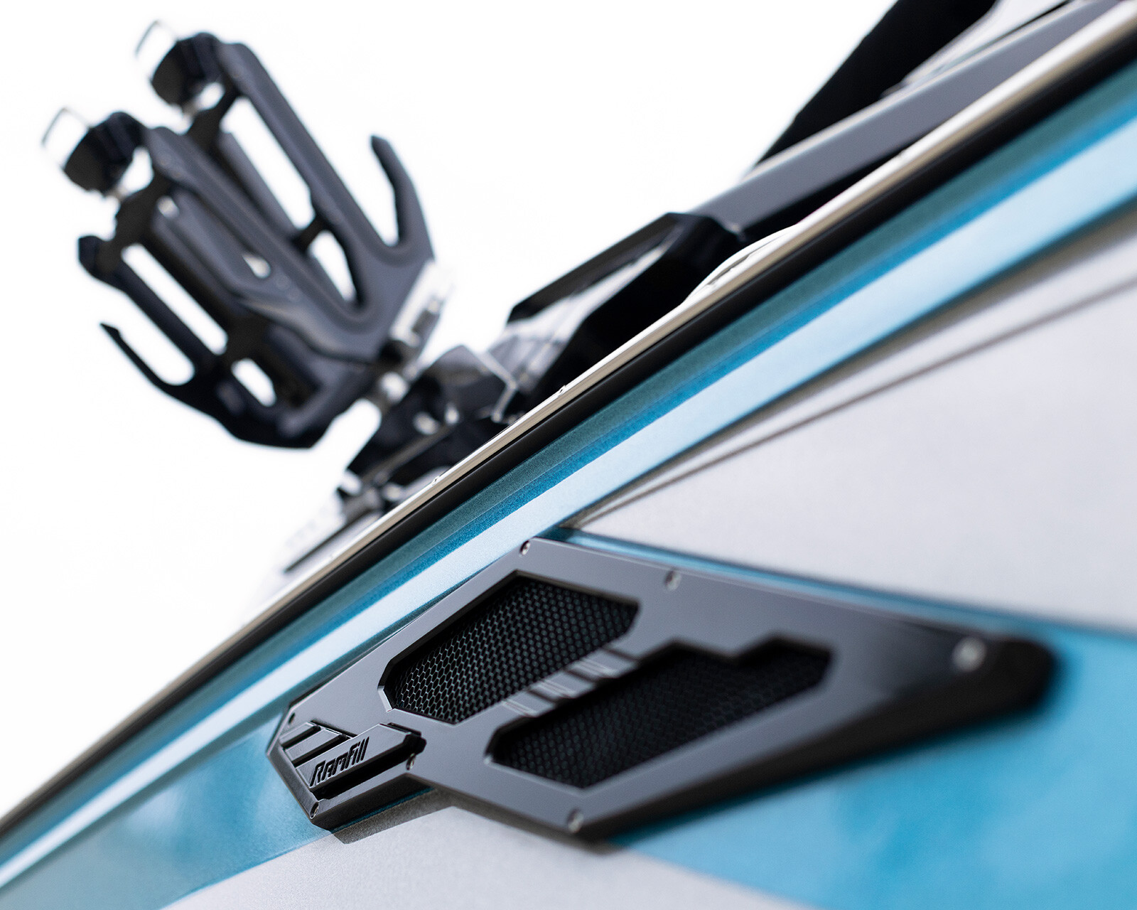 Close-up of a blue and gray Centurion Ri245 with a black metal vent and a mounted wakeboard rack against a white background.