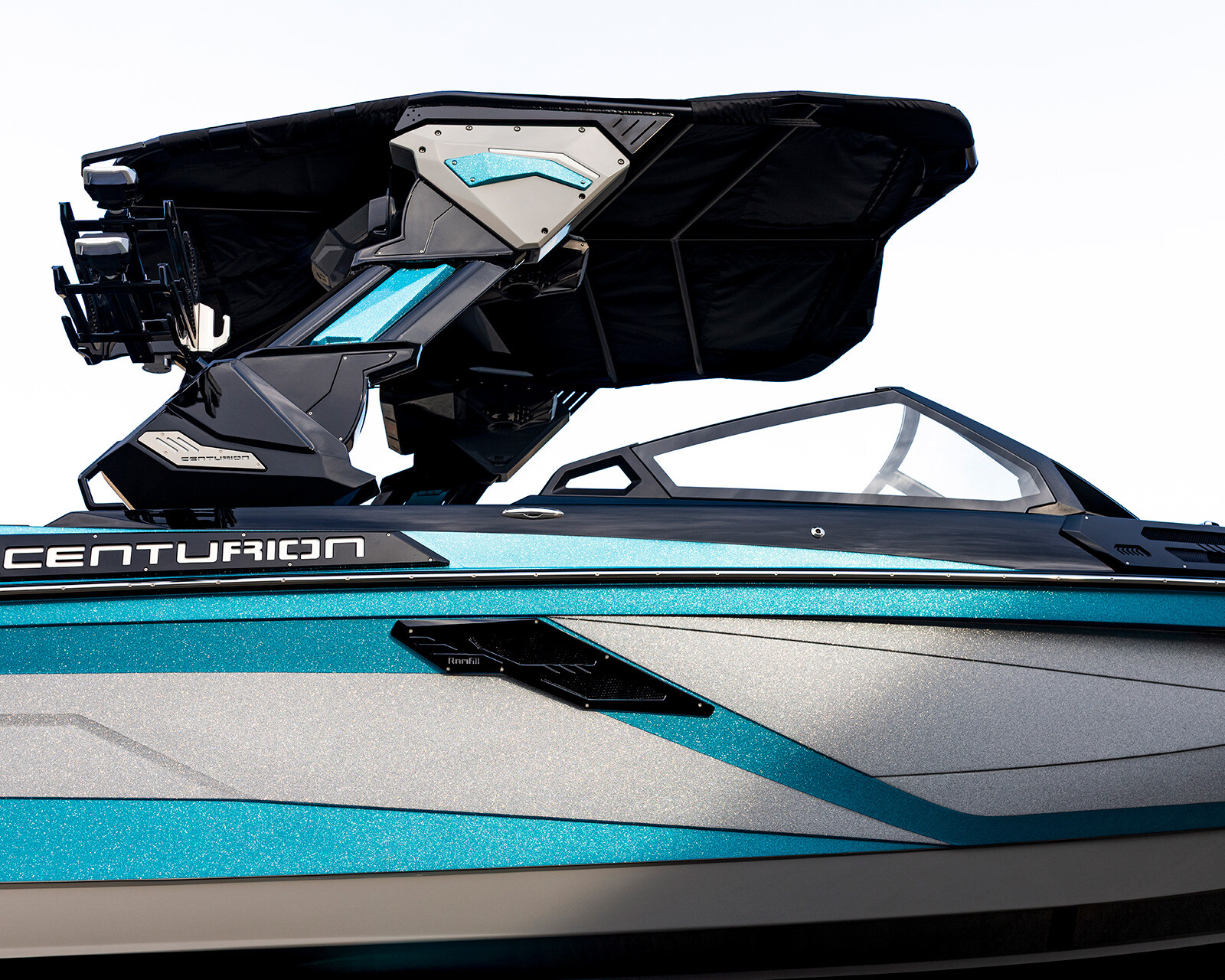 A close-up view of a modern Centurion Ri245 Surf Boat in blue and gray, featuring a wakeboard tower and windshield against a white background.