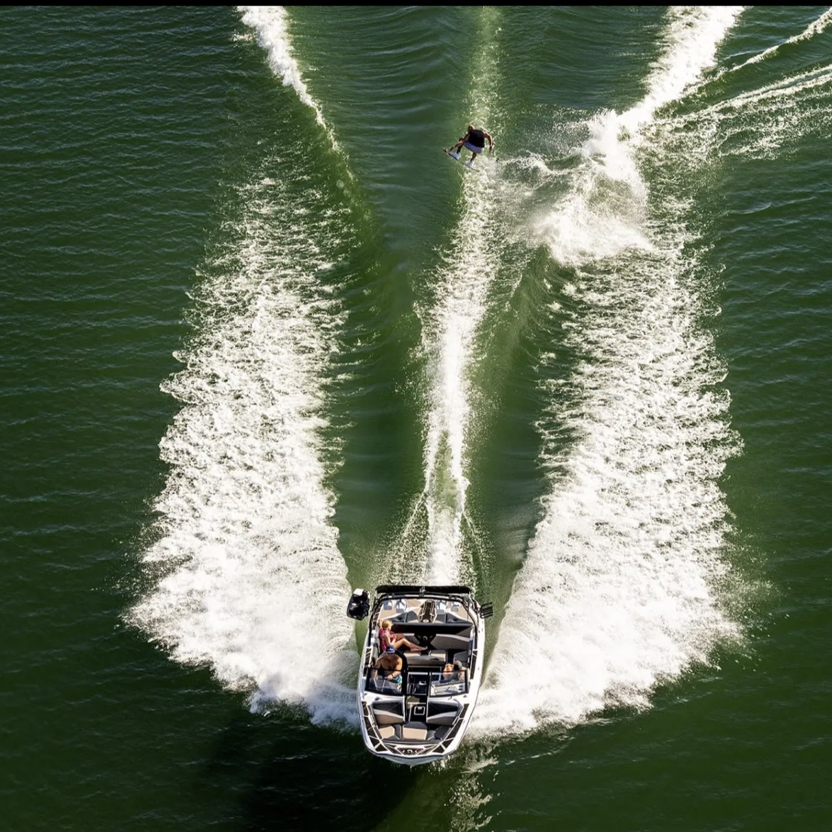A speedboat creates wake patterns on green water while towing a wakeboarder behind it.