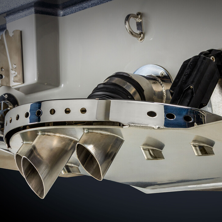 Close-up of a boat's stainless steel exhaust system and through-hull fittings mounted on the transom, with visible hose connections and mechanical components.