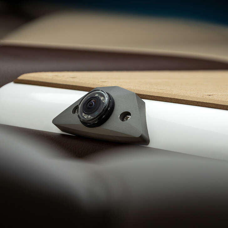 Close-up of a small camera mounted on a white and beige surface, with screws securing it in place.