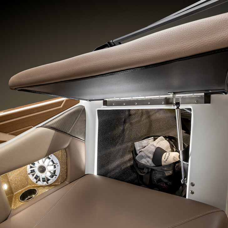 Open storage compartment under a brown cushioned seat, revealing a bag inside; speaker and cup holder are visible on the side panel.