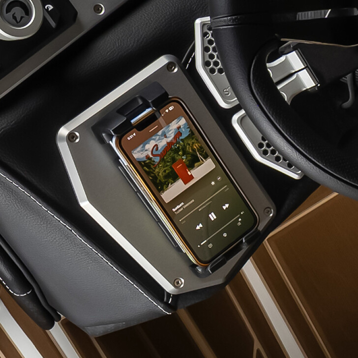 A smartphone displays a music app and is securely placed in a mounted holder on a vehicle dashboard next to the steering wheel.