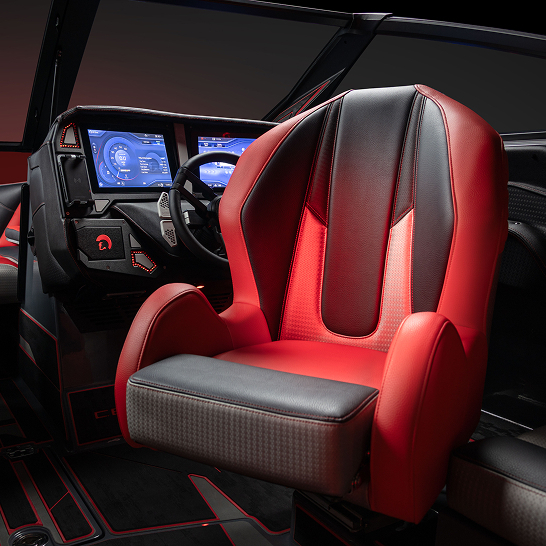 A modern Ri Series captain's chair in a boat cockpit, upholstered in red and black, with digital control screens and an illuminated dashboard in the background to Make The Features Personal.