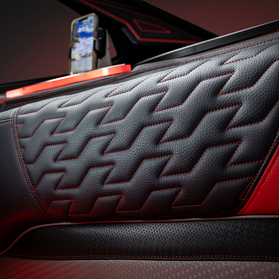 Close-up of a Ri Series car door panel with black and red leather, showcasing a zigzag stitched pattern and personalized features, with a mounted smartphone visible in the background.