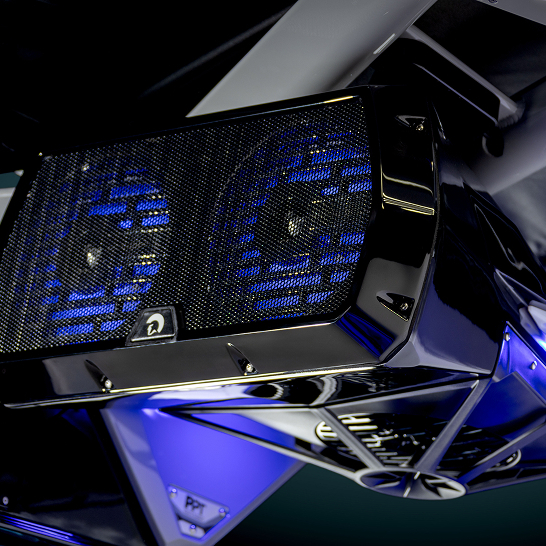 Close-up view of a black and chrome Ri Series dual speaker system with blue LED lighting, mounted under a surface. Features personal audio controls for a tailored listening experience.