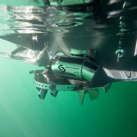 Underwater view of a boat propeller fitted with a metallic Centurion-branded device, part of the Ri Series, partially submerged in green-tinted water.