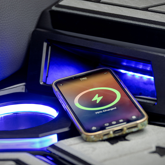 A smartphone is wirelessly charging on a Ri Series charging pad inside a car console, with blue LED lights illuminating the area and showcasing its Features Personal capabilities.
