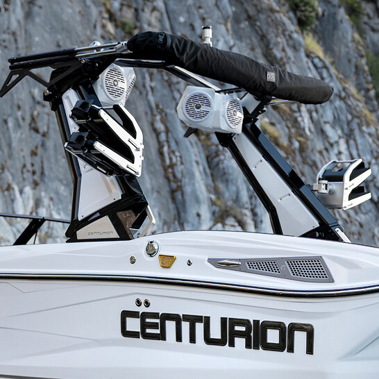 Close-up of a white Centurion boat with black trim and Nv Series mounted speakers, highlighting Features Personal touches against a dramatic rocky cliff backdrop.