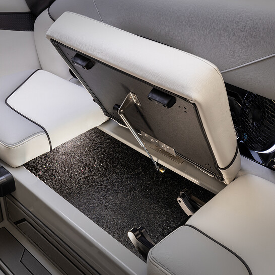 A car interior from the NV Series shows a rear seat lifted up to reveal a storage compartment underneath, highlighting personal storage features, visible metal hinges, and textured black flooring.
