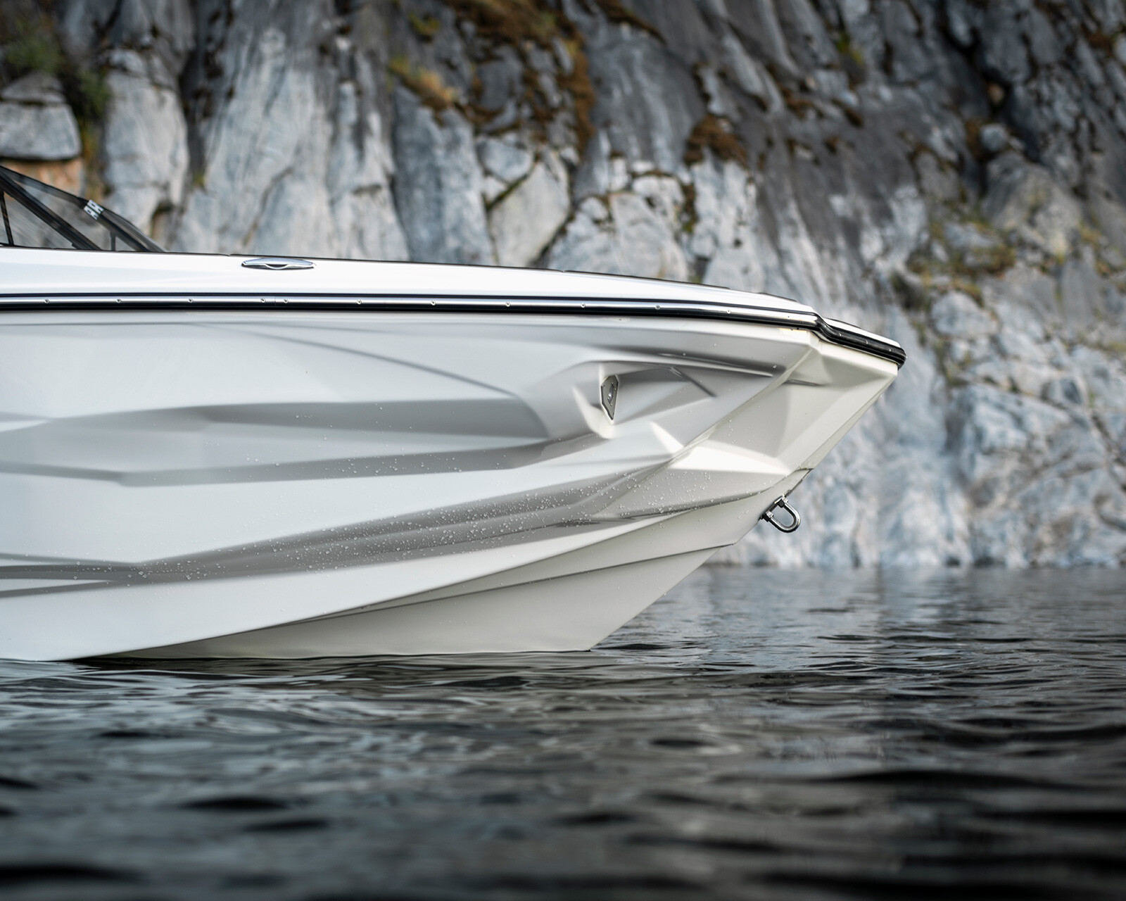 The bow of a white Centurion Nv213 is shown on calm water with a rocky cliff in the background.