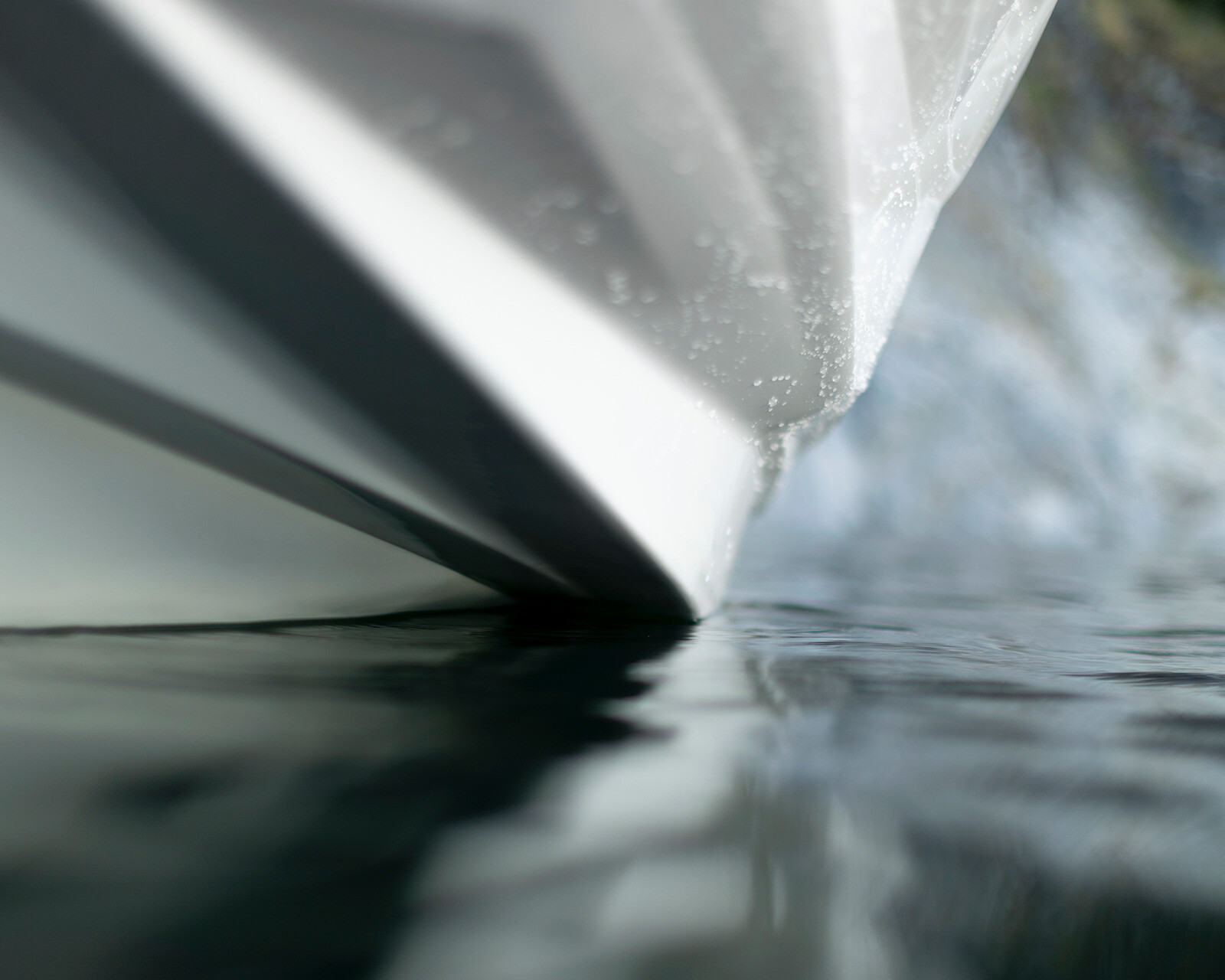 Close-up view of the bow of a Centurion Nv213 cutting through calm water, with a blurred shoreline in the background.