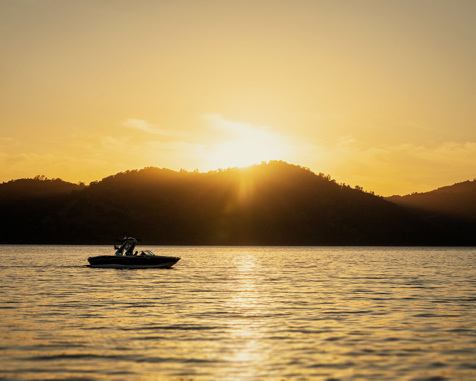 A Centurion Nv233 floats on calm water at sunset, with hills silhouetted in the background and the sun low in the sky.