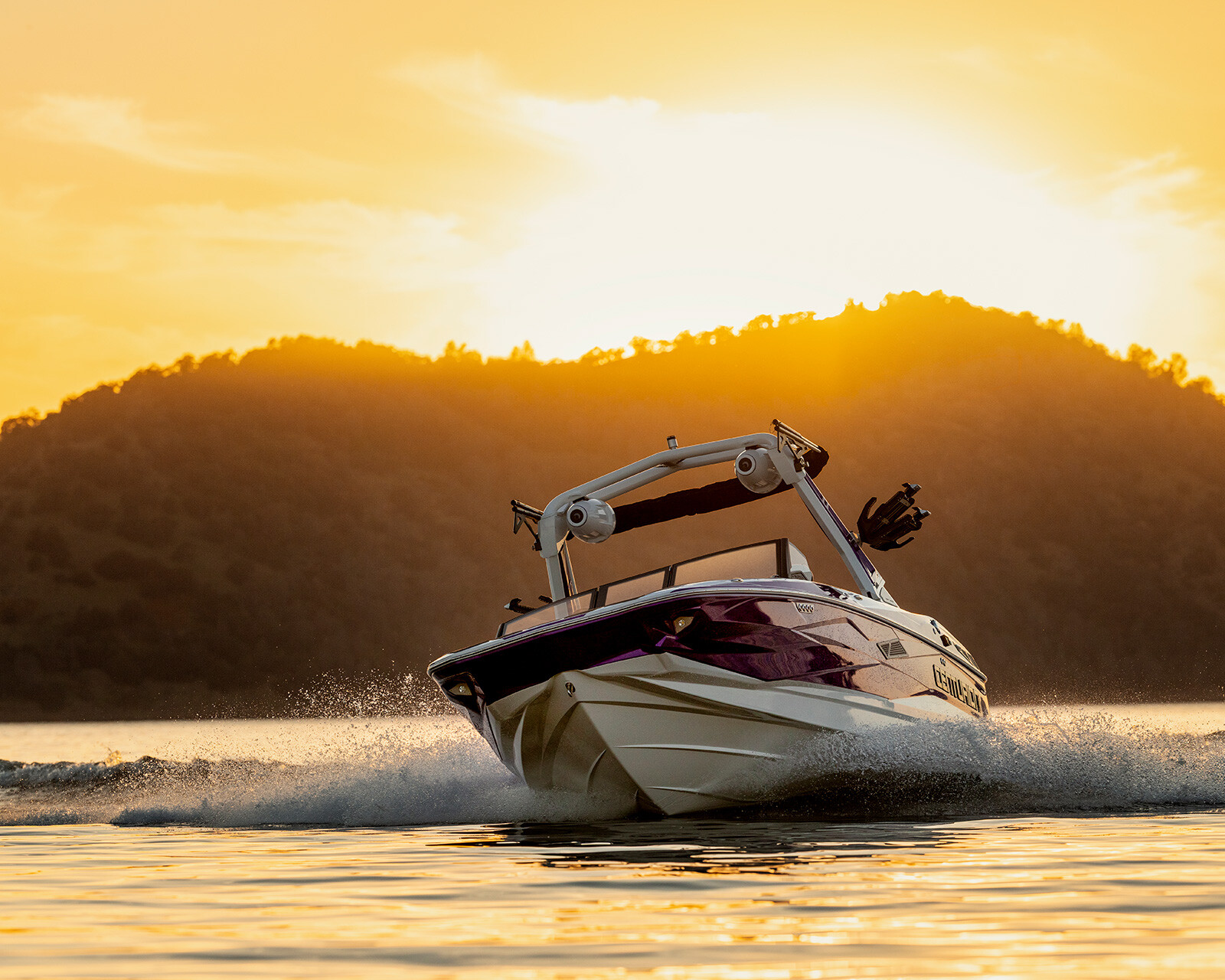 A Centurion Nv233 glides quickly across the water at sunset, with hills in the background and sunlight reflecting off the lake.