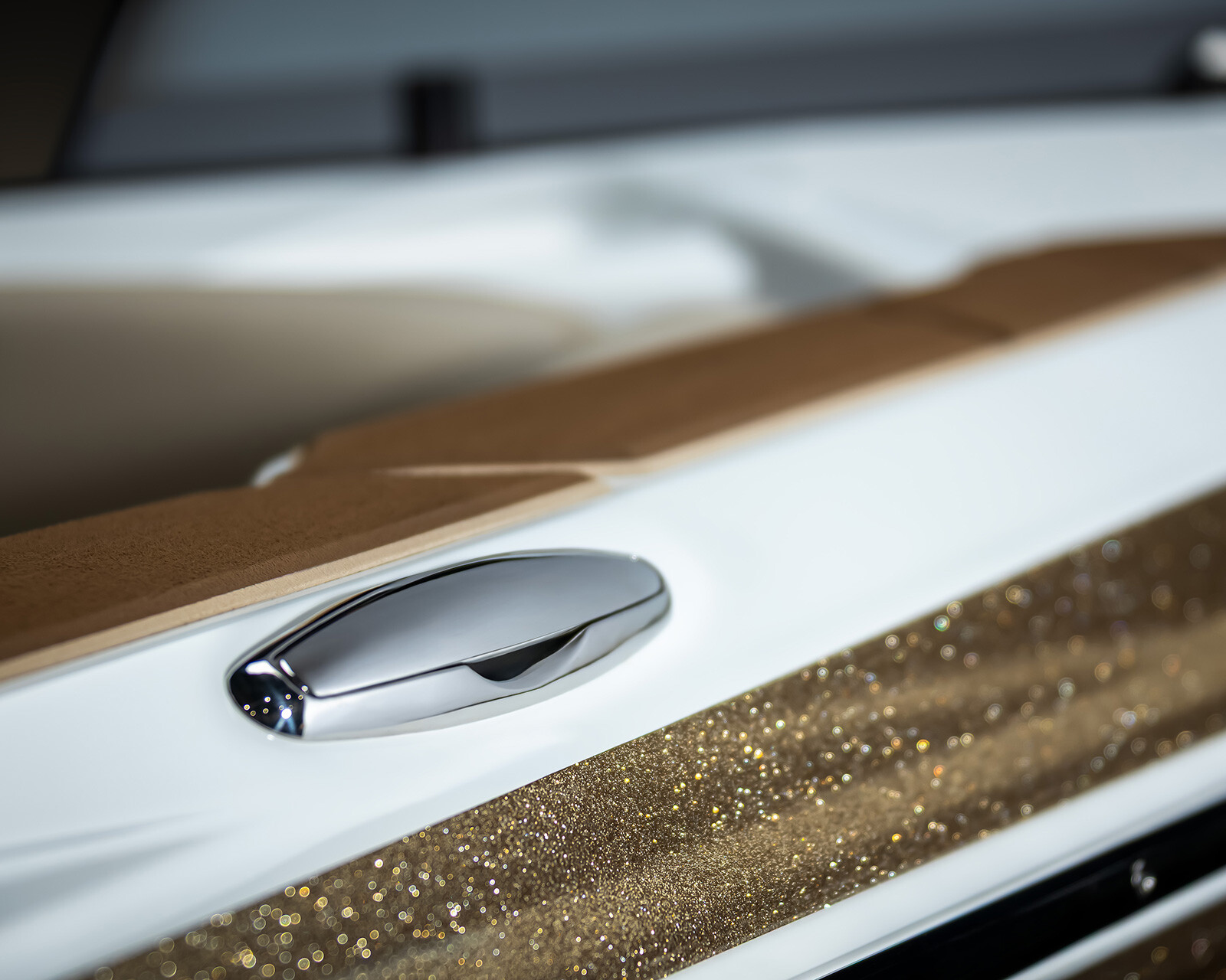 Close-up of a Centurion Nv213 Wake Boat’s side featuring a metallic door handle, white trim, tan upholstery, and a sparkling gold panel.