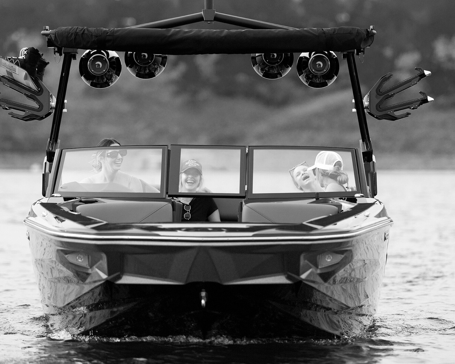 A group of four people sit smiling in a modern Nv233 Surf Boat on the water, photographed from the front.