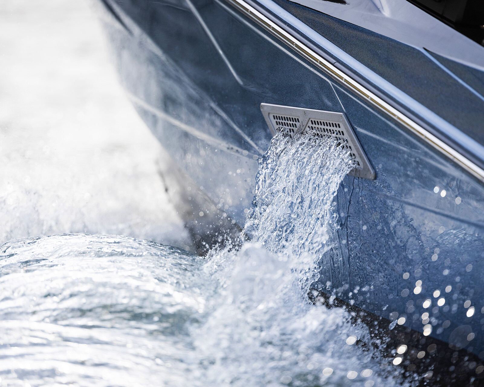 Close-up of water being discharged from a drain on the side of a moving Centurion Nv233, with splashing water visible around the hull.