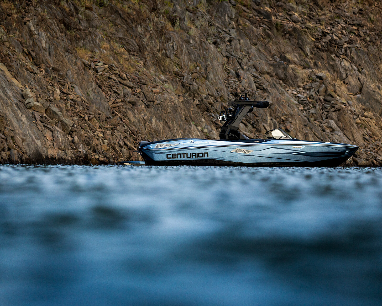 A gray Nv233 Surf Boat floats on calm water near a rocky shoreline.