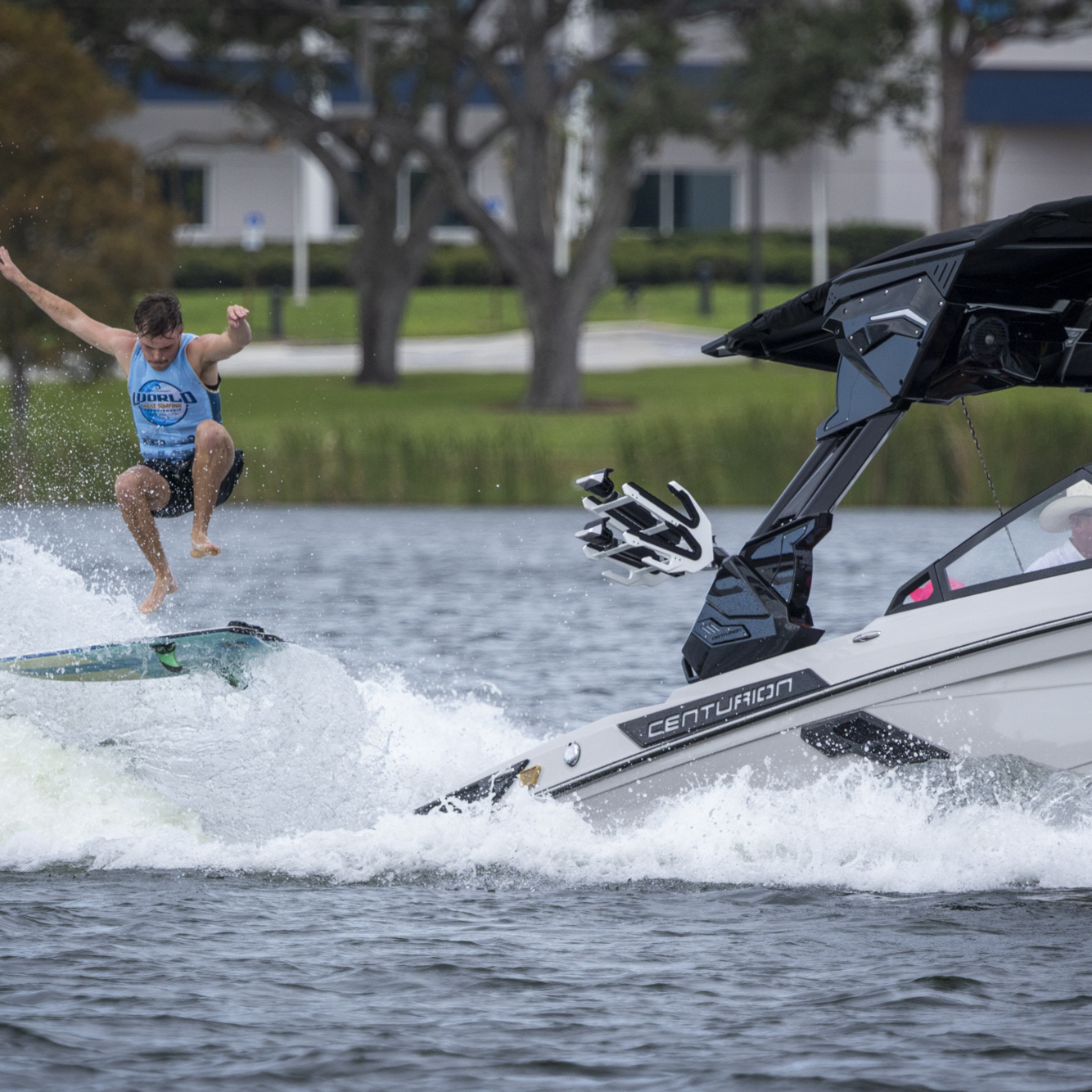 A person wakesurfs behind a motorboat, performing a jump on the water while the boat moves forward.