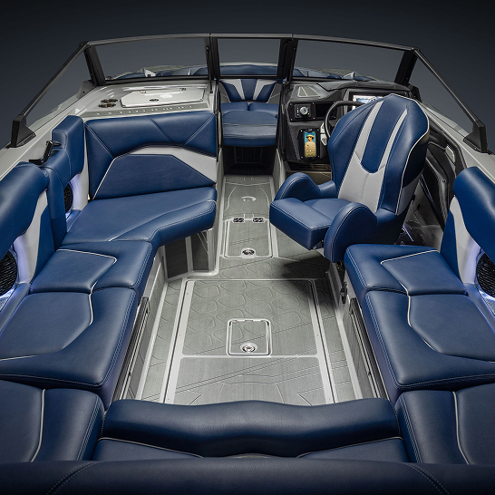 Modern boat interior with blue and gray cushioned seating, a captain’s chair, control panel, cup holders, and a textured floor.