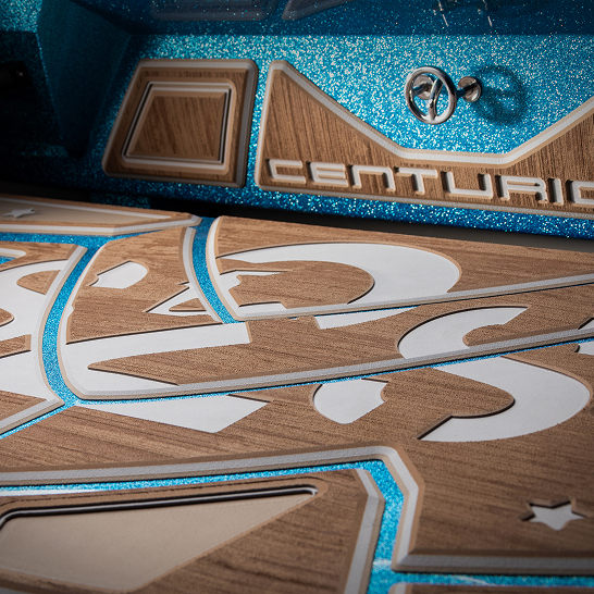 Close-up of a boat deck with a geometric pattern, wood and white detailing, blue glitter accents, and a “Centurion” logo on the side panel.