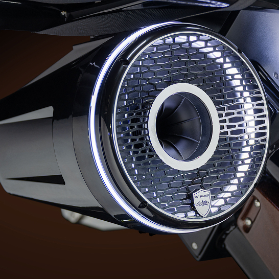 Close-up view of a black cylindrical speaker with a mesh grille, circular LED light accent, and a logo that reads 