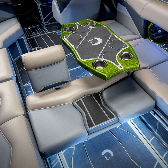 Modern boat interior with grey and blue cushioned seating, a green and black hexagonal table with cup holders, and detailed flooring.