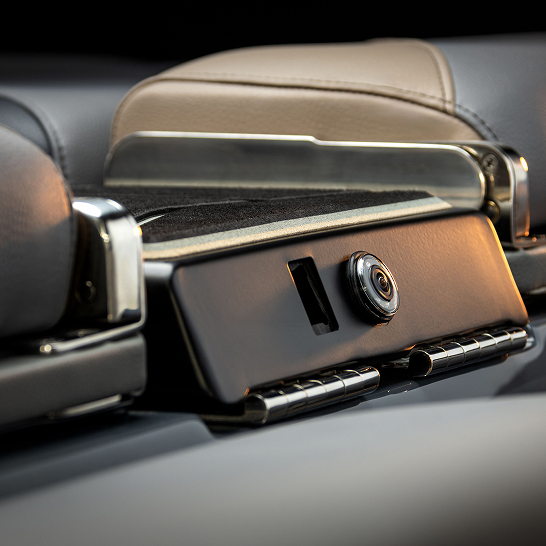 Close-up of a car’s rearview camera mounted between two headrests, with part of the vehicle's interior upholstery visible.