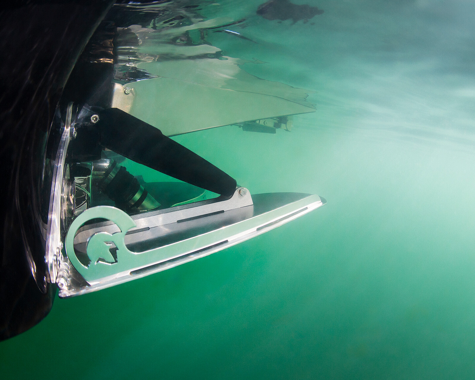 Close-up underwater view of a metallic Centurion Nv243 wake boat propeller and rudder partially submerged in clear greenish water.