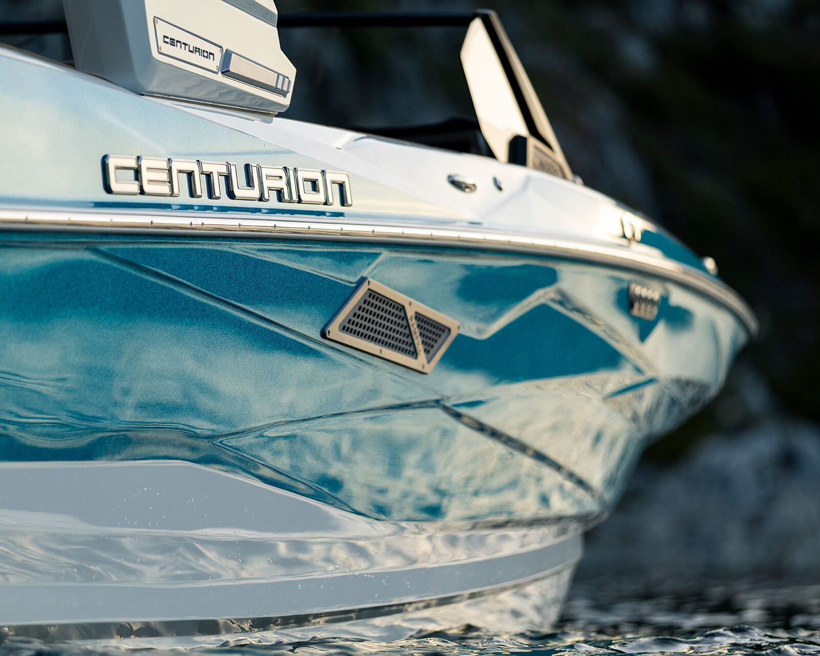 Close-up of the bow of a blue and white Centurion Nv243 Surf Boat, showing the brand logo and part of the hull above water.