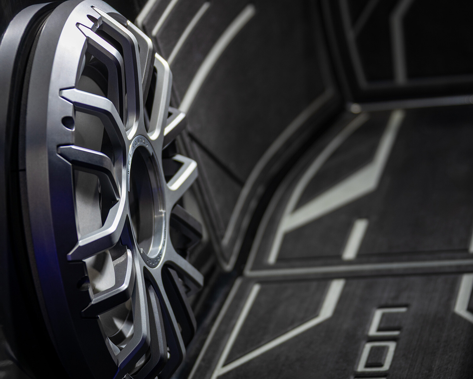 Close-up view of a silver alloy car wheel rim mounted on a dark, geometric-patterned background, resembling the modern design seen on Centurion Nv243 models.