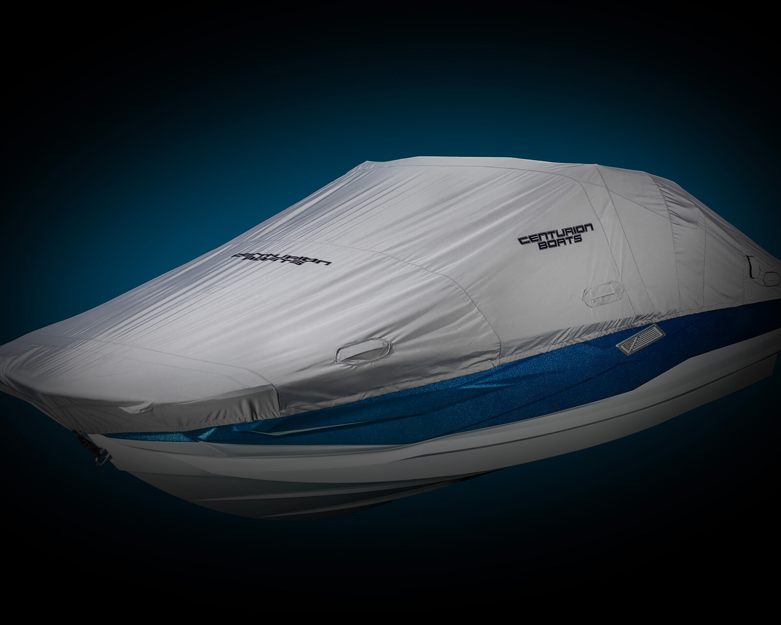 A blue and white Nv243 Wake Boat is fully covered with a fitted, gray Centurion Boats protective cover against a dark background.