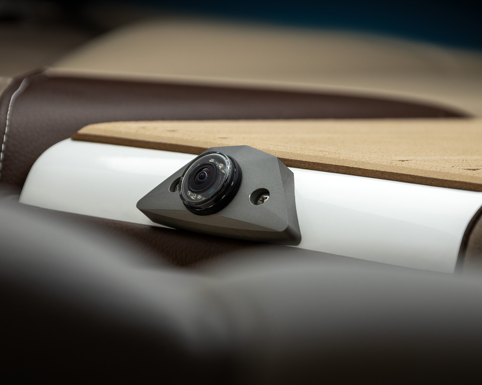 Close-up of a small camera embedded in a beige and brown surface, likely part of a Centurion Nv243 Wake Boat’s interior.