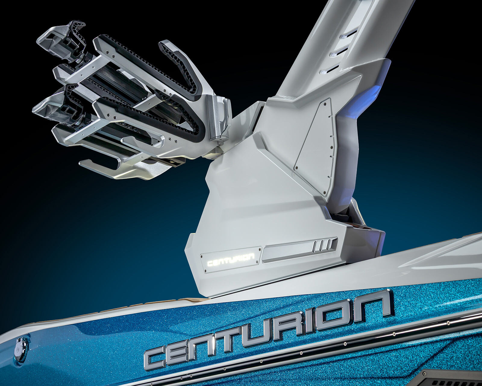 Close-up view of a sleek, blue and white Centurion Nv243 wake boat featuring a modern wakeboard tower with racks against a dark background.