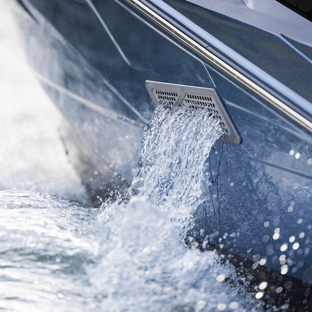 Close-up of water pouring out of a rectangular drain on the side of a boat into the surrounding water.