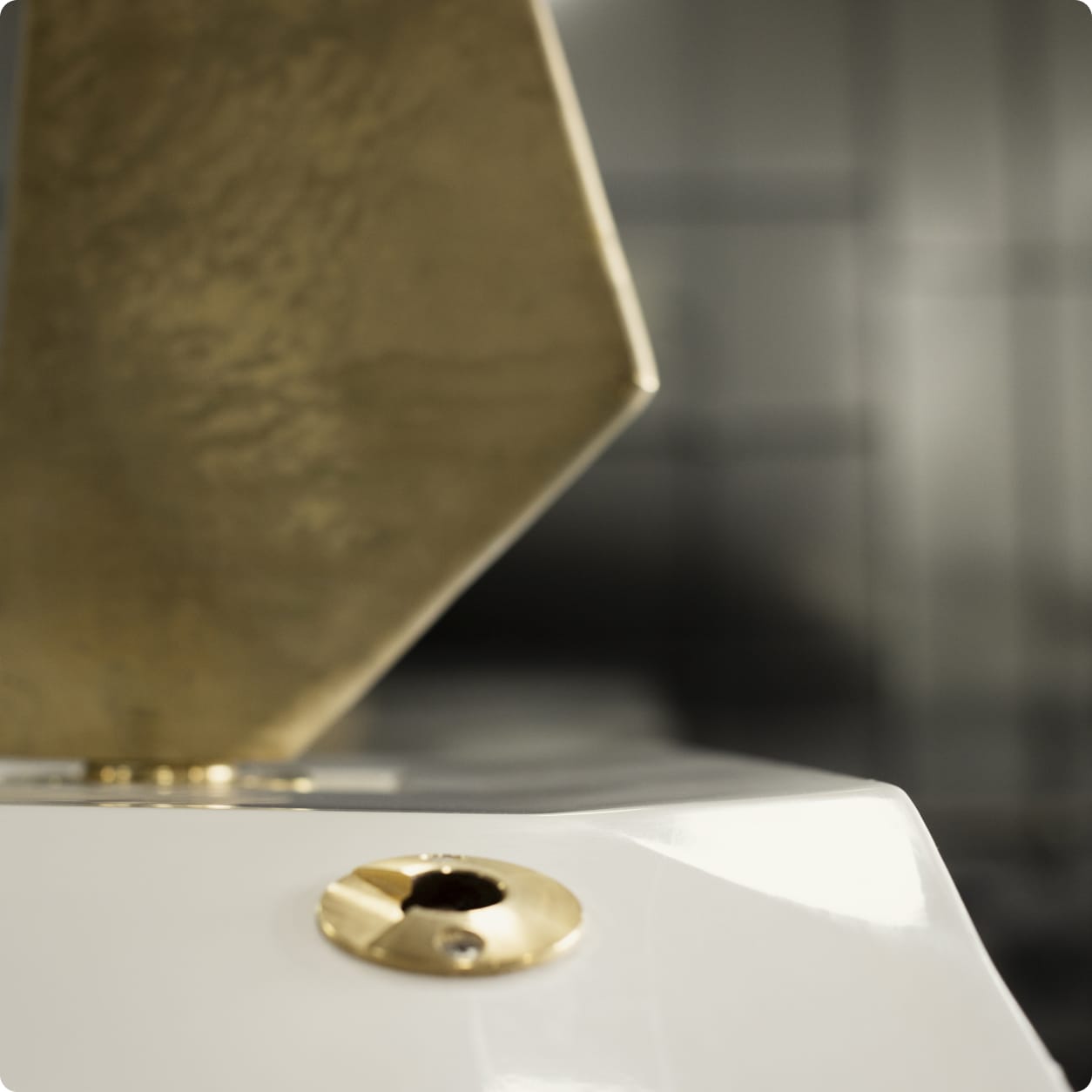 Close-up of a white surface with a Centurion Opti-V Hull gold metal fitting in the foreground and a blurred brass geometric object in the background.
