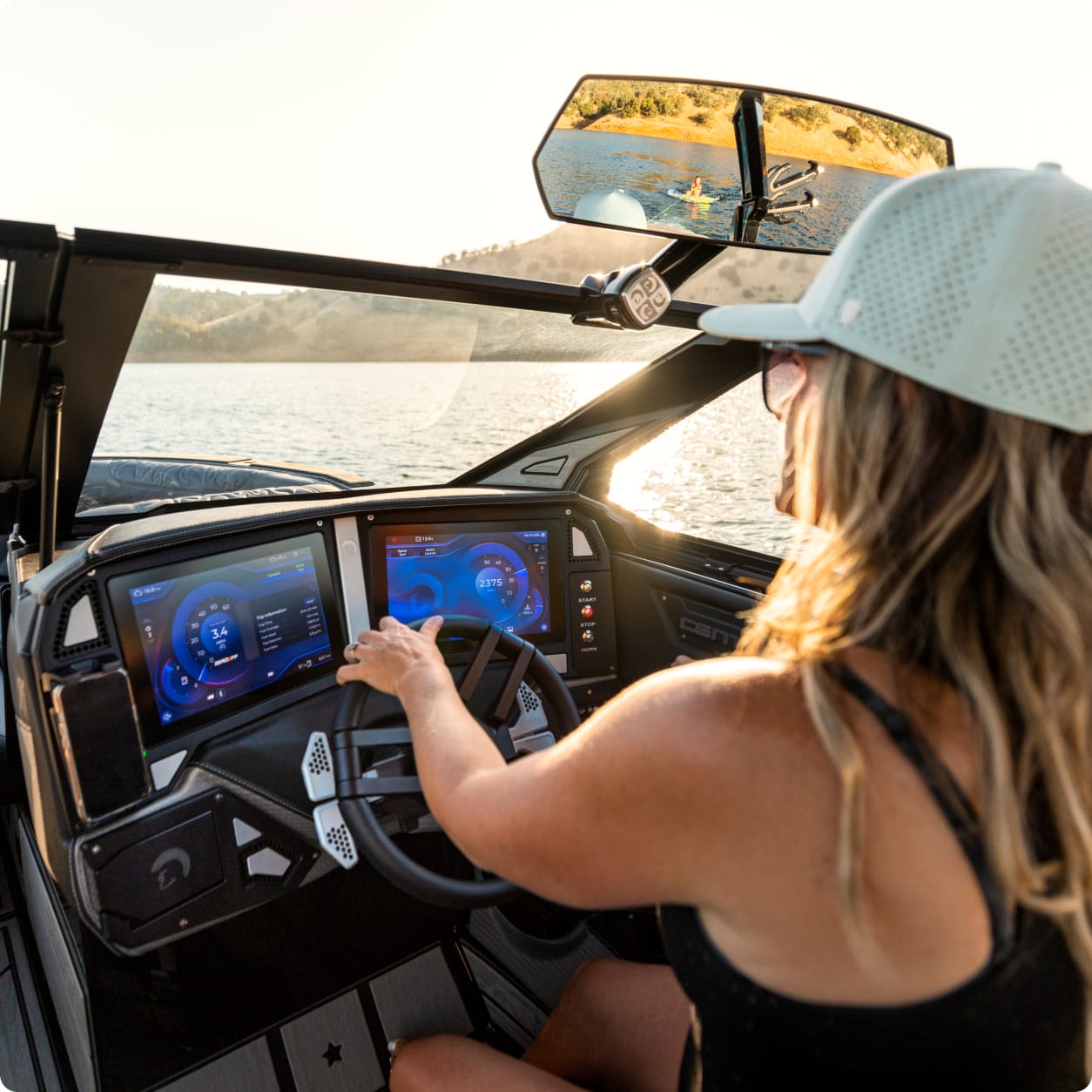 A woman wearing a cap operates a modern boat with Centurion Ballast using digital touchscreen controls while on a lake during daylight.