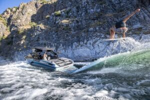 A person rides a wakeboard and jumps on a wave created by a Ri245 boat, with rocky cliffs in the background, enjoying unforgettable time on the water.