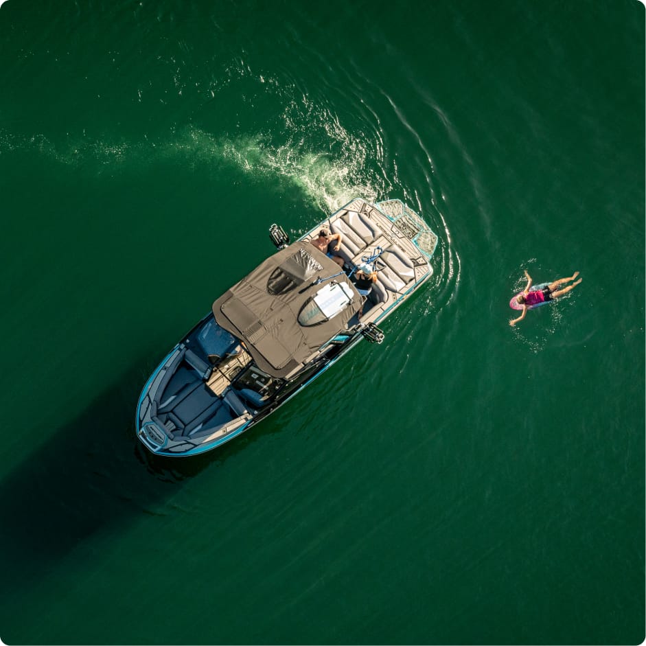 Aerial view of a Centurion Opti-V Hull boat on green water with a person swimming nearby, leaving a wake behind the boat.