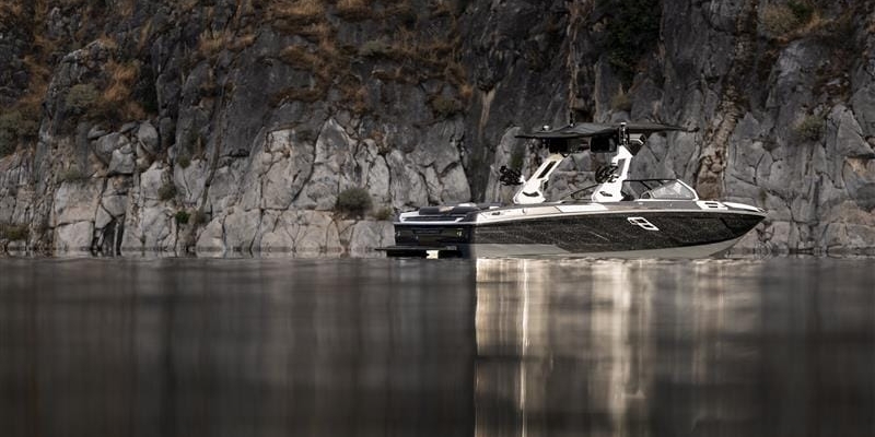 A black and white motorboat is moored on calm water near a rocky cliff with sparse vegetation.